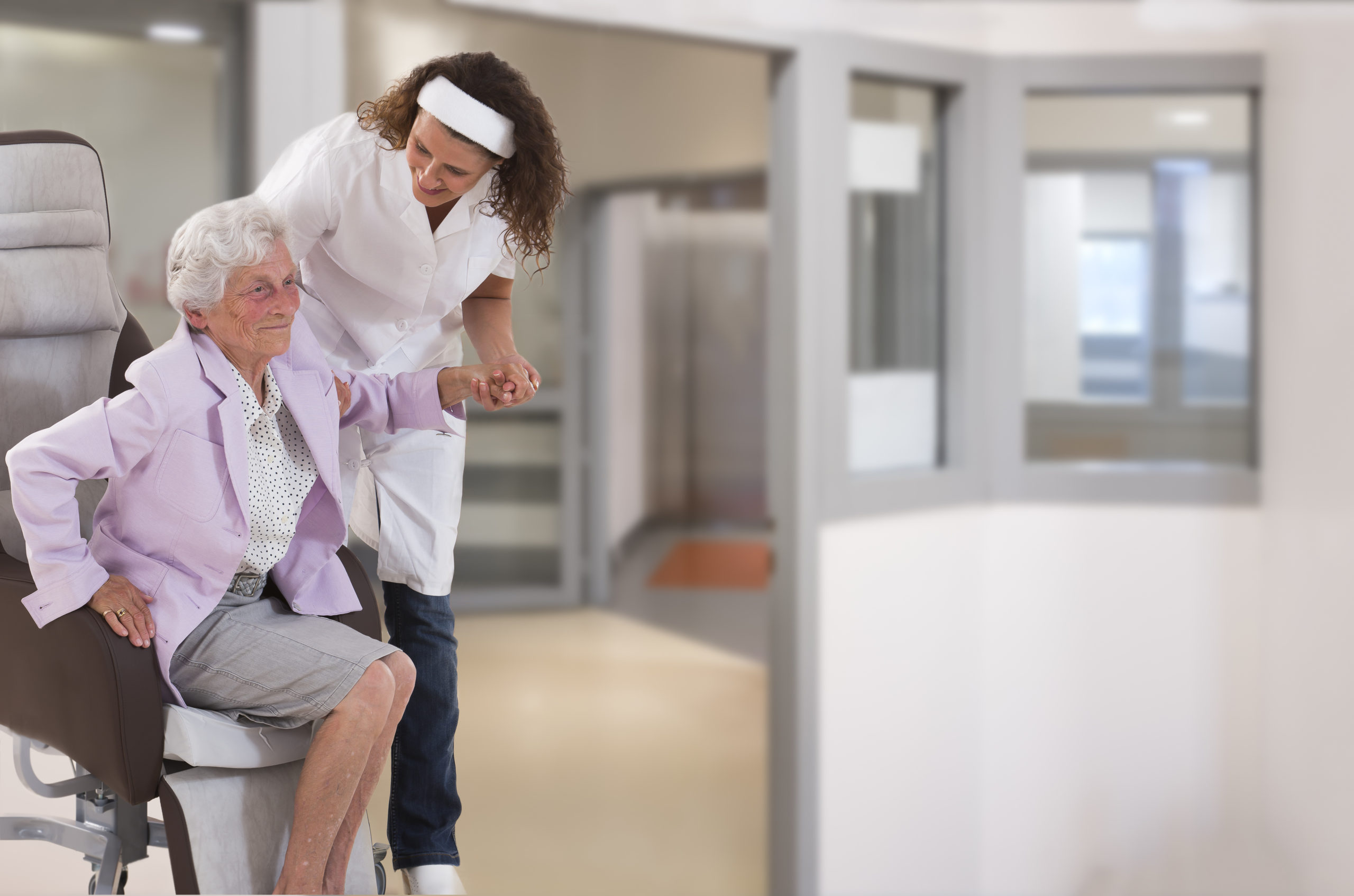 Nurse Helping Disabled Lady In Getting Up In Large, Windows, Background, Coridor